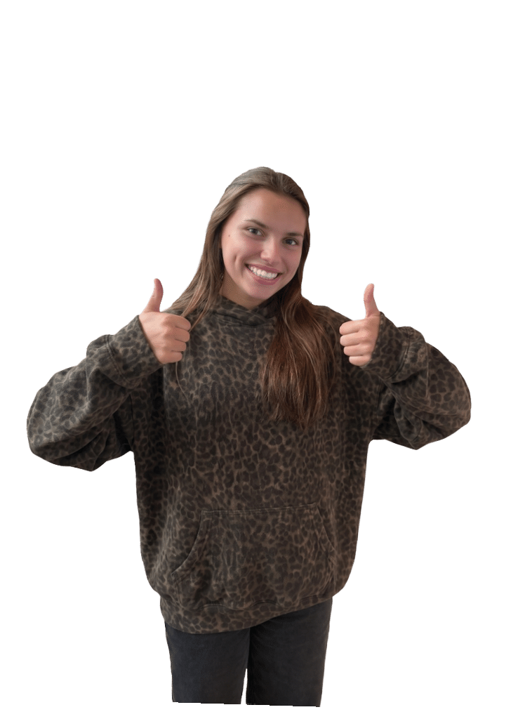A Berkeley College student with long hair wearing a loose, patterned sweater is smiling and giving two thumbs up.
