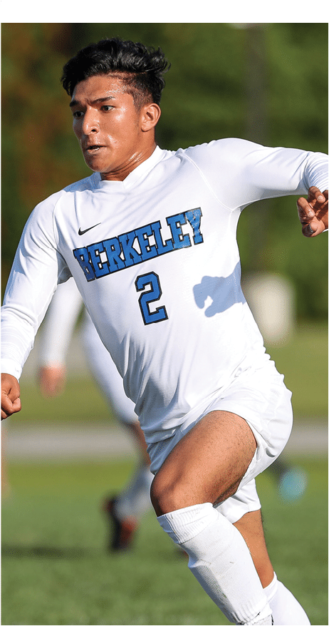 A Berkeley College student wearing a white Berkeley soccer uniform with the number 2 is running on a grassy field.