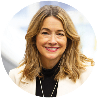 Berkeley College faculty member Andrea Kennedy with shoulder-length wavy hair is smiling and wearing a light-colored blazer over a black top with a necklace. 