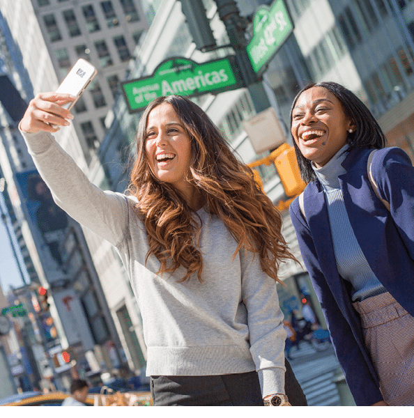 Berkeley College New York City students with long hair are smiling and taking a selfie on a city street near a sign that reads Avenue of the Americas 