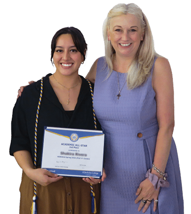 Two adults stand closely together smiling, with one holding an academic award certificate and wearing a graduation stole. 